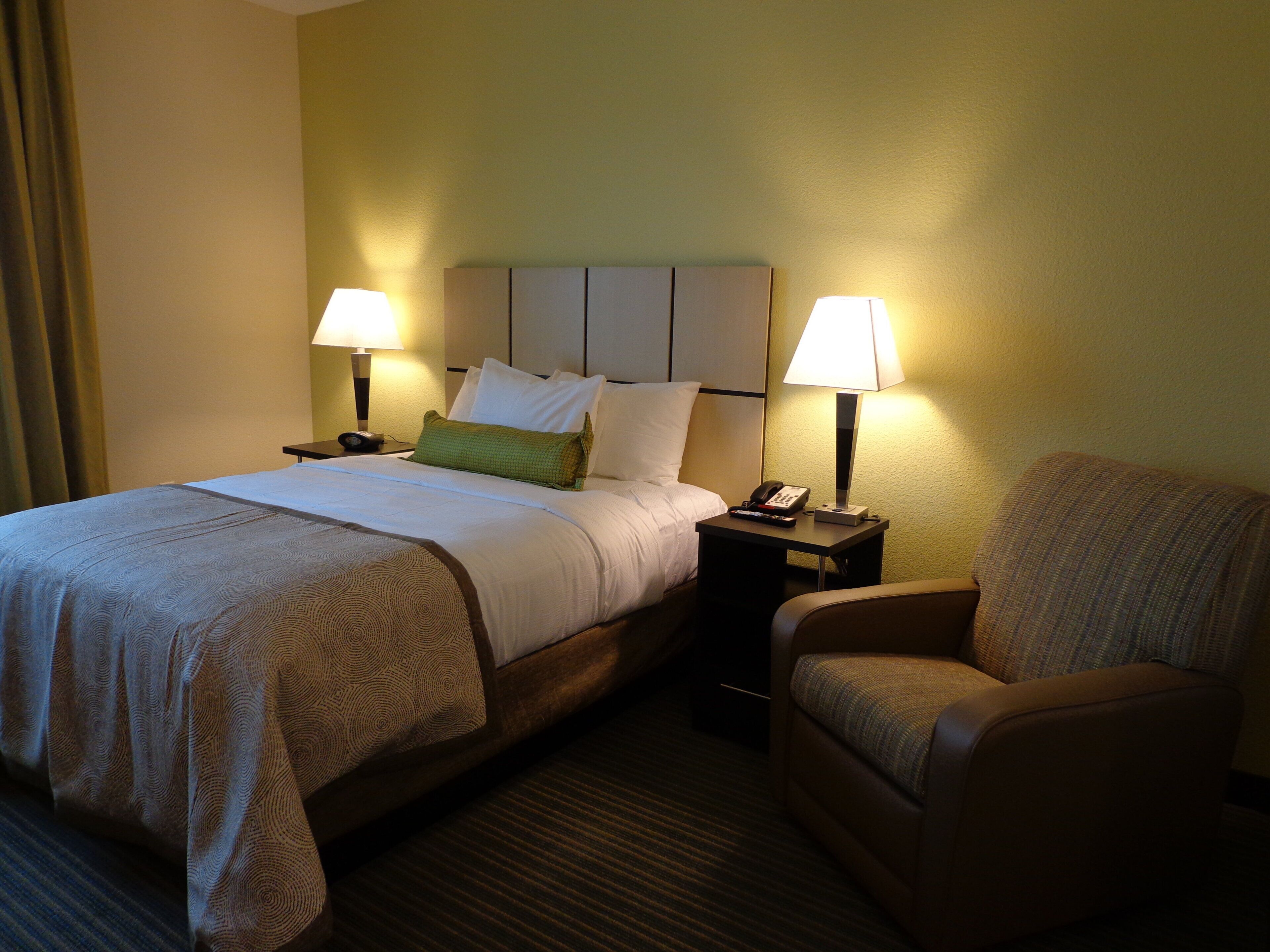 A hotel room with a bed, two bedside lamps, a chair, and a nightstand with a telephone.