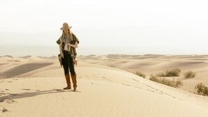 Una persona de pie sobre una duna de arena, con un extenso paisaje desértico al fondo.