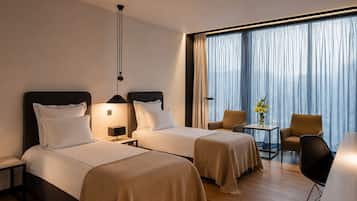 A hotel room with two beds, a small table with a vase, and a chair.