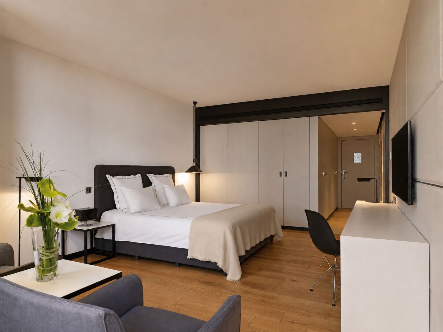 Una habitación de hotel moderna con cama, mesita de noche, silla, escritorio y televisor en la pared.