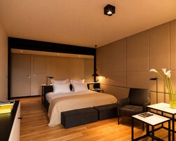 A modern bedroom with a bed, bedside tables, a chair, a small table, and a vase with flowers.