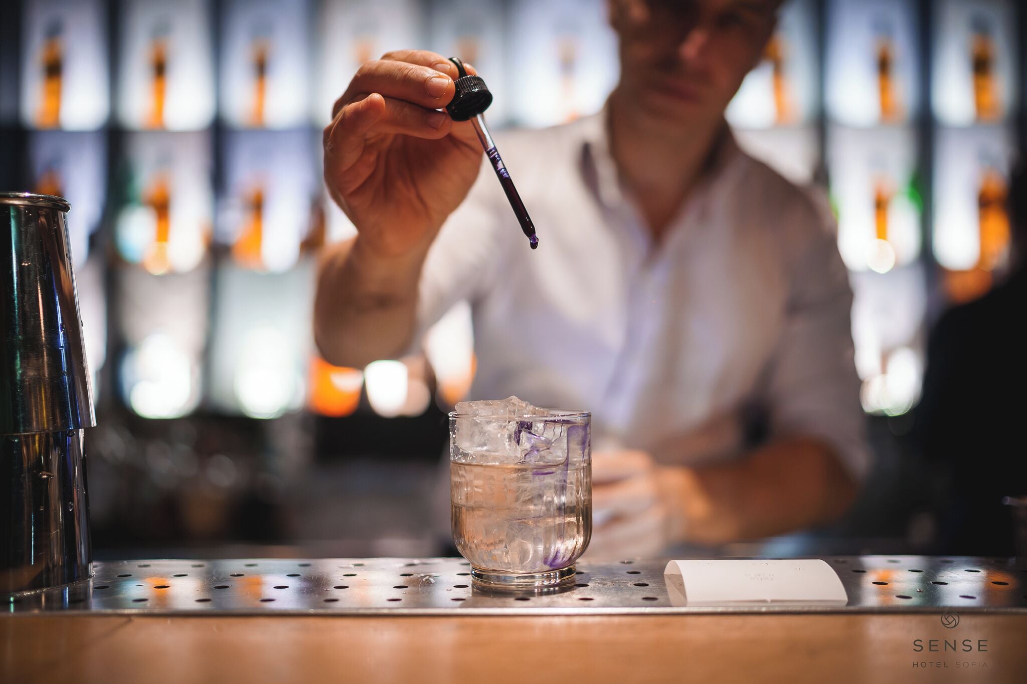 Un bar avec un barman, un verre d’eau avec des glaçons et une bouteille d’alcool.