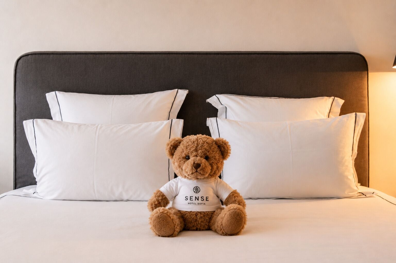 A bed with white pillows and a brown teddy bear sitting on it.
