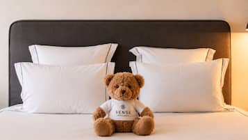 A bed with white pillows and a brown teddy bear sitting on it.