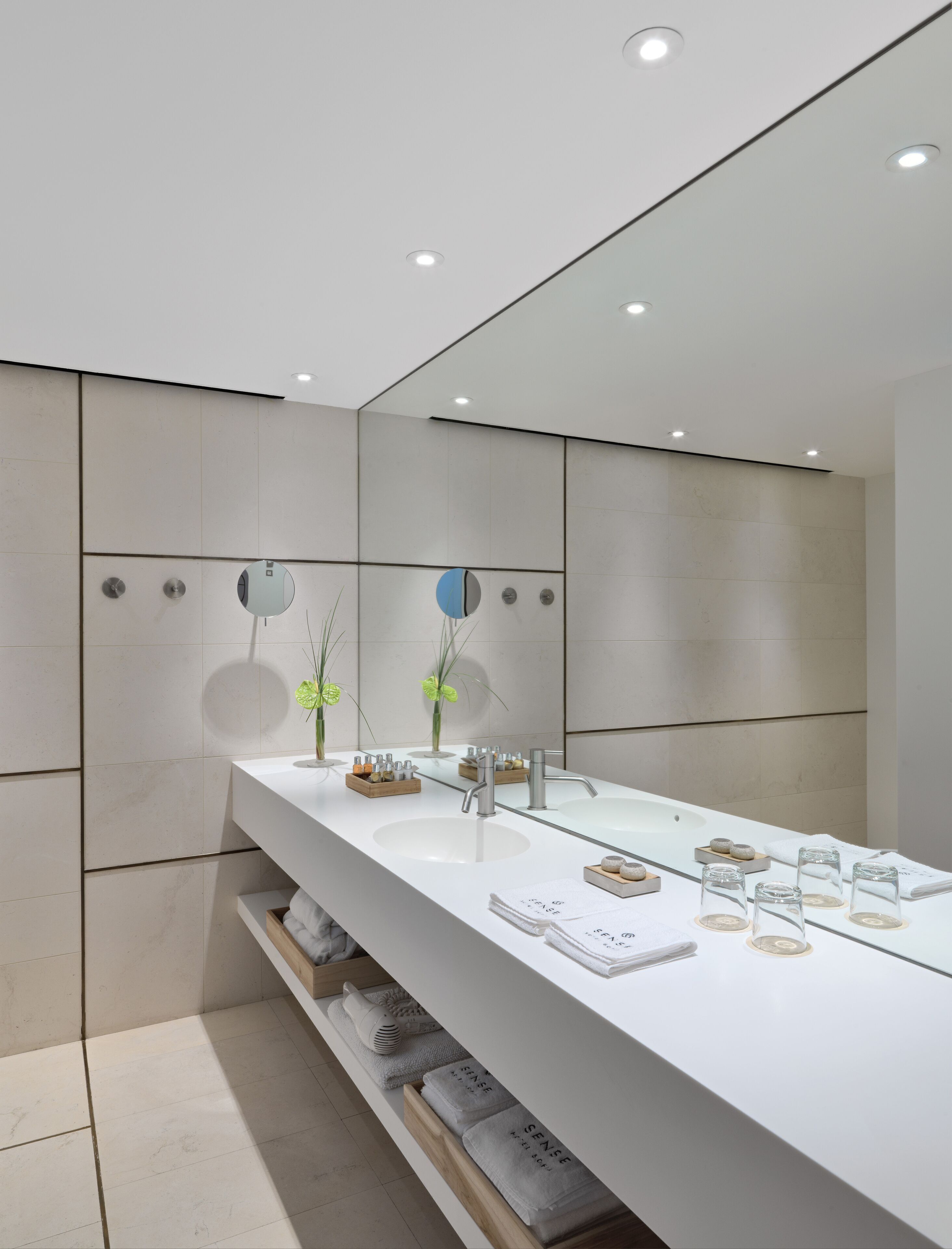 A modern bathroom with a large mirror, two sinks, and a vanity with toiletries.