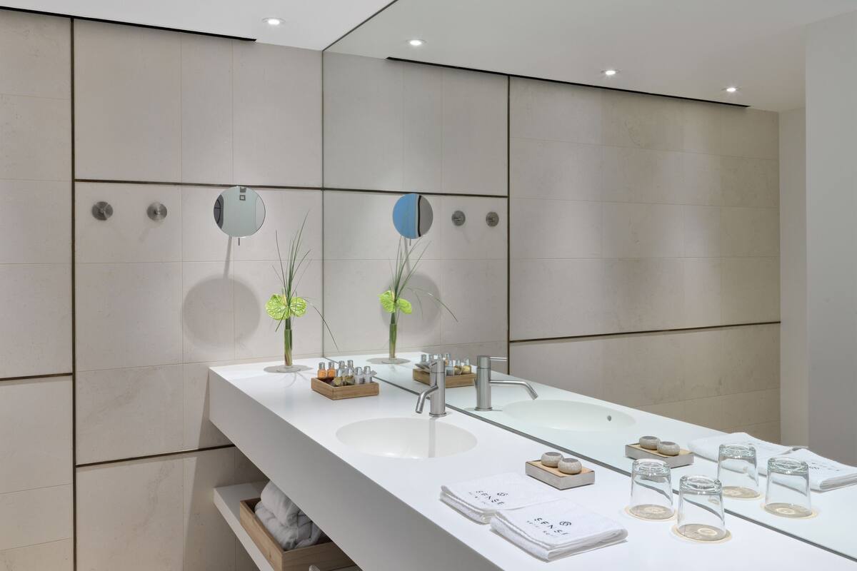 A modern bathroom with a large mirror, two sinks, and a vanity with toiletries.