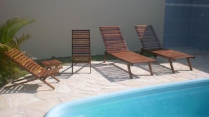 A poolside area with wooden lounge chairs and a tiled wall. - Pousada Cabufa (Cabo Frio)