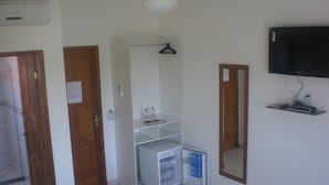 A hotel room with a bed, a TV mounted on the wall, a wardrobe, and a small refrigerator. - Pousada Cabufa (Cabo Frio)