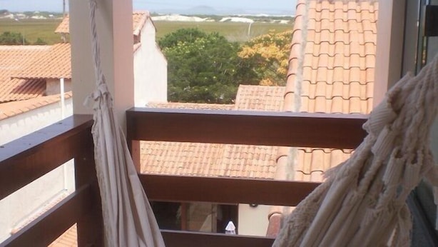 A balcony with a hammock, a view of buildings, and a clear sky. - Pousada Cabufa (Cabo Frio)