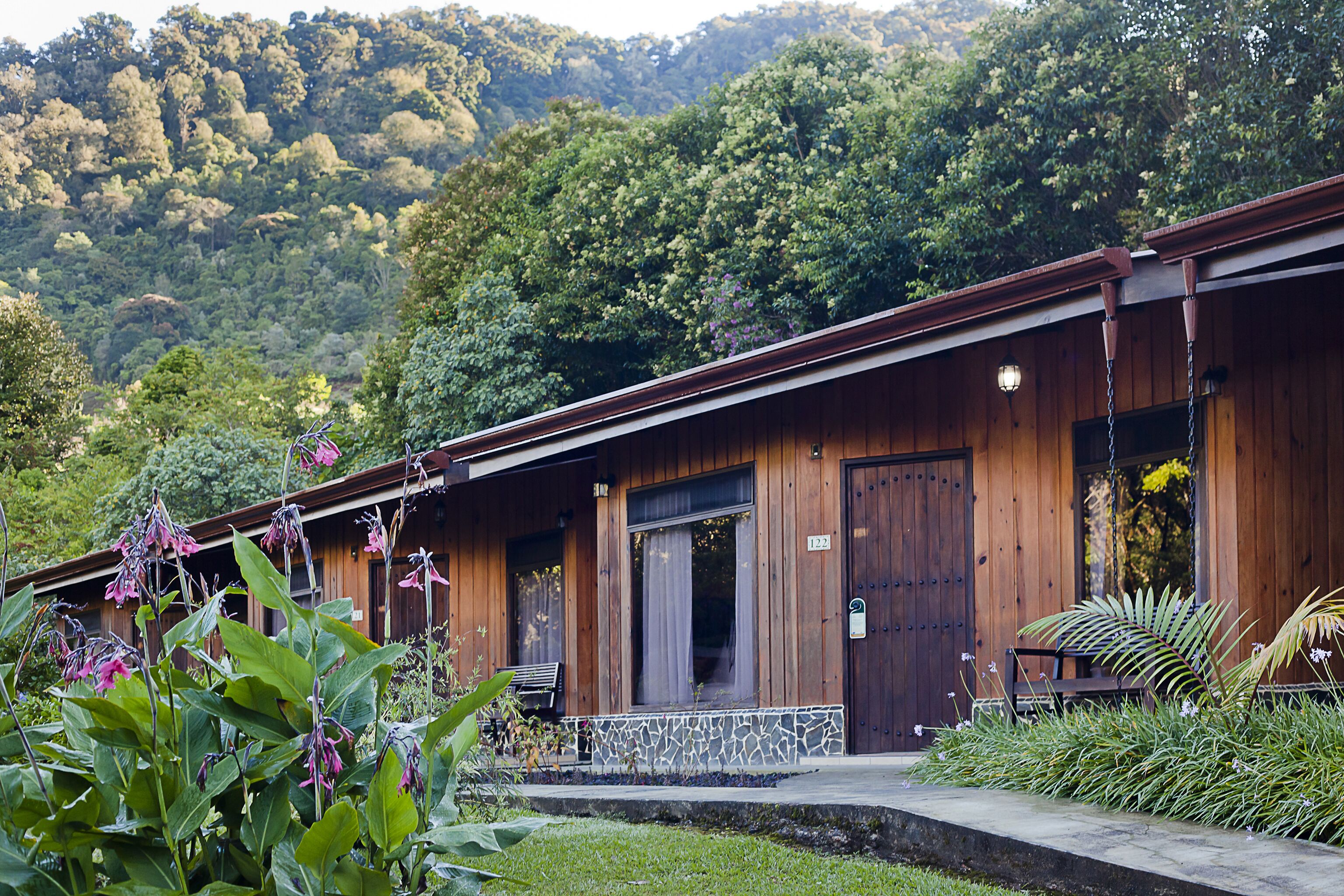 Eine Holzhütte mit Veranda, umgeben von üppigem Grün und einem bewaldeten Hang.