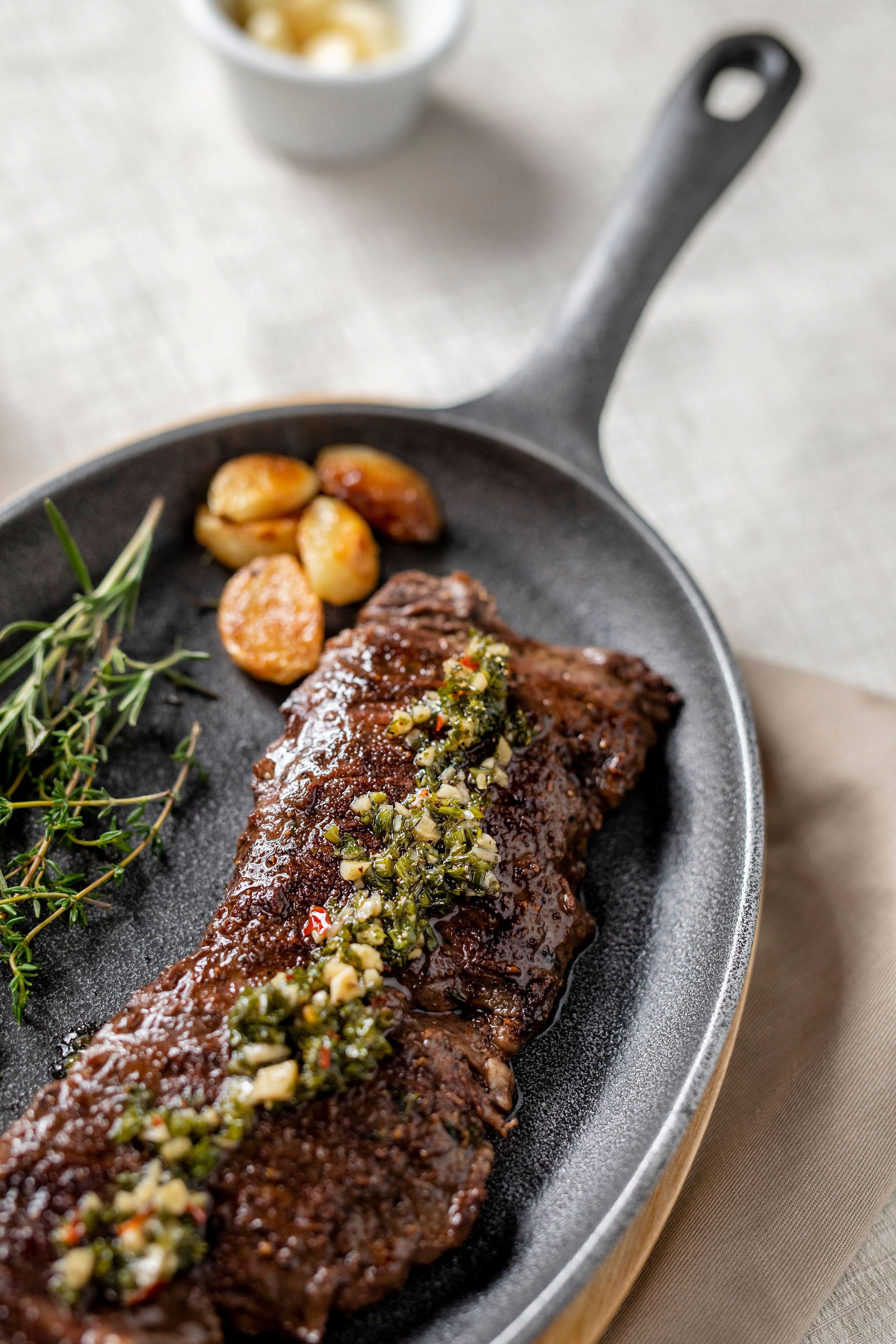 Bistec con cobertura de hierbas verdes y papas asadas en una sartén.