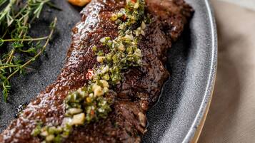 Bistec con cobertura de hierbas verdes y papas asadas en una sartén.