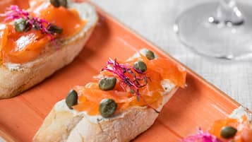 Three open-faced sandwiches with smoked salmon, capers, and pink edible flowers on a rectangular orange plate.