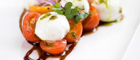 A white rectangular plate with a food arrangement consisting of cherry tomatoes, mozzarella balls, and a drizzle of sauce.