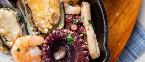 Un plato de mariscos con mejillones, camarones y pulpo, servido con pan sobre una tabla de madera.