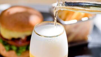 A glass of white wine being poured into a stemmed glass. In the background, there is a burger on a plate.