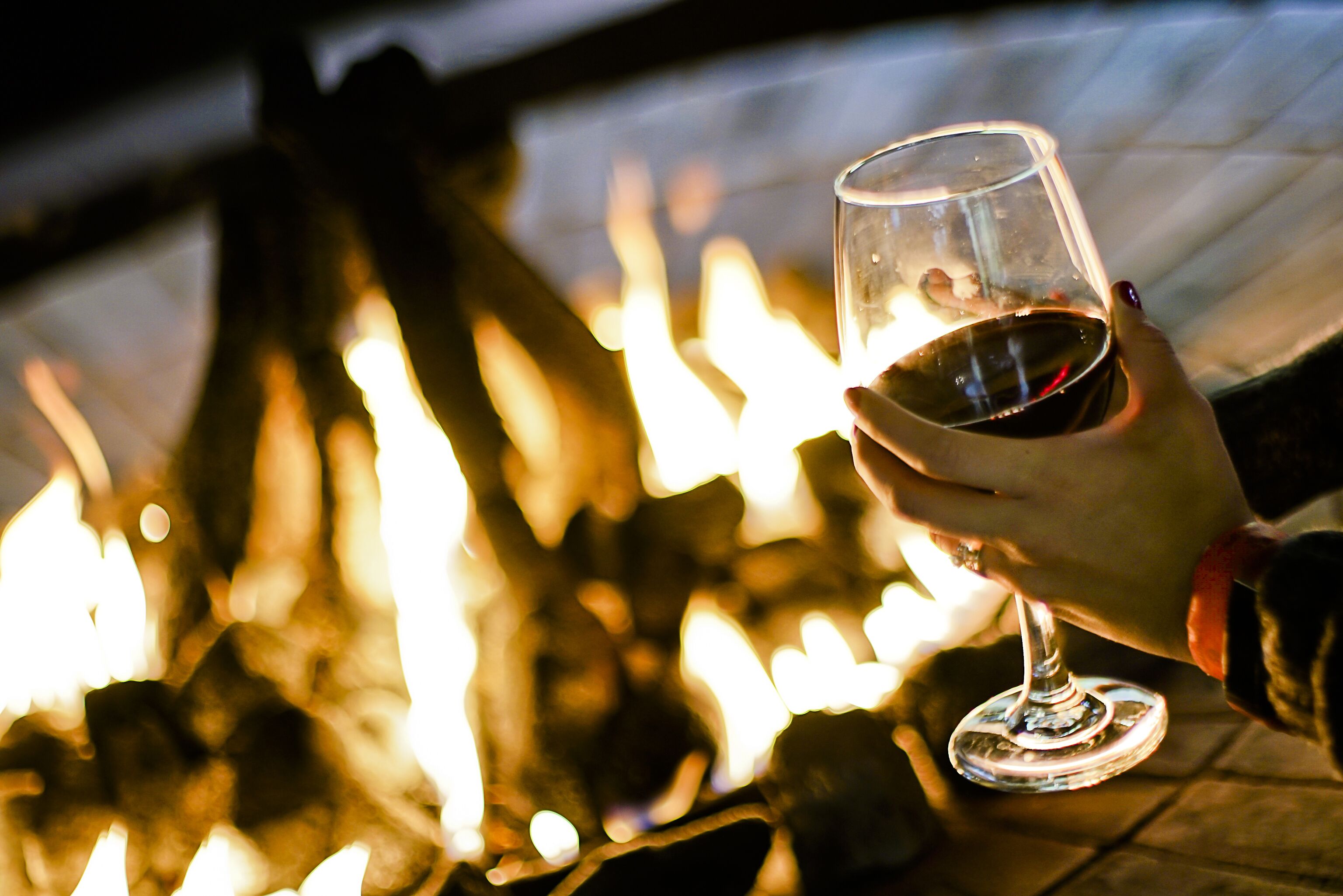 Une main tenant un verre de vin, avec un feu en arrière-plan.