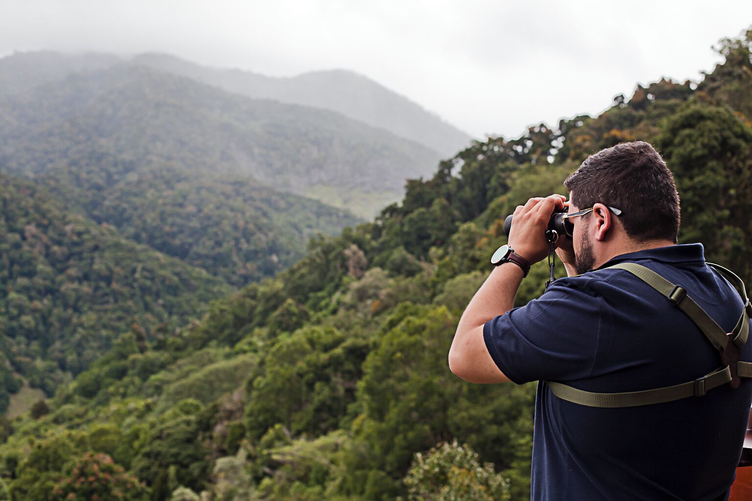 A person taking a photograph of a mountainous landscape with dense greenery.