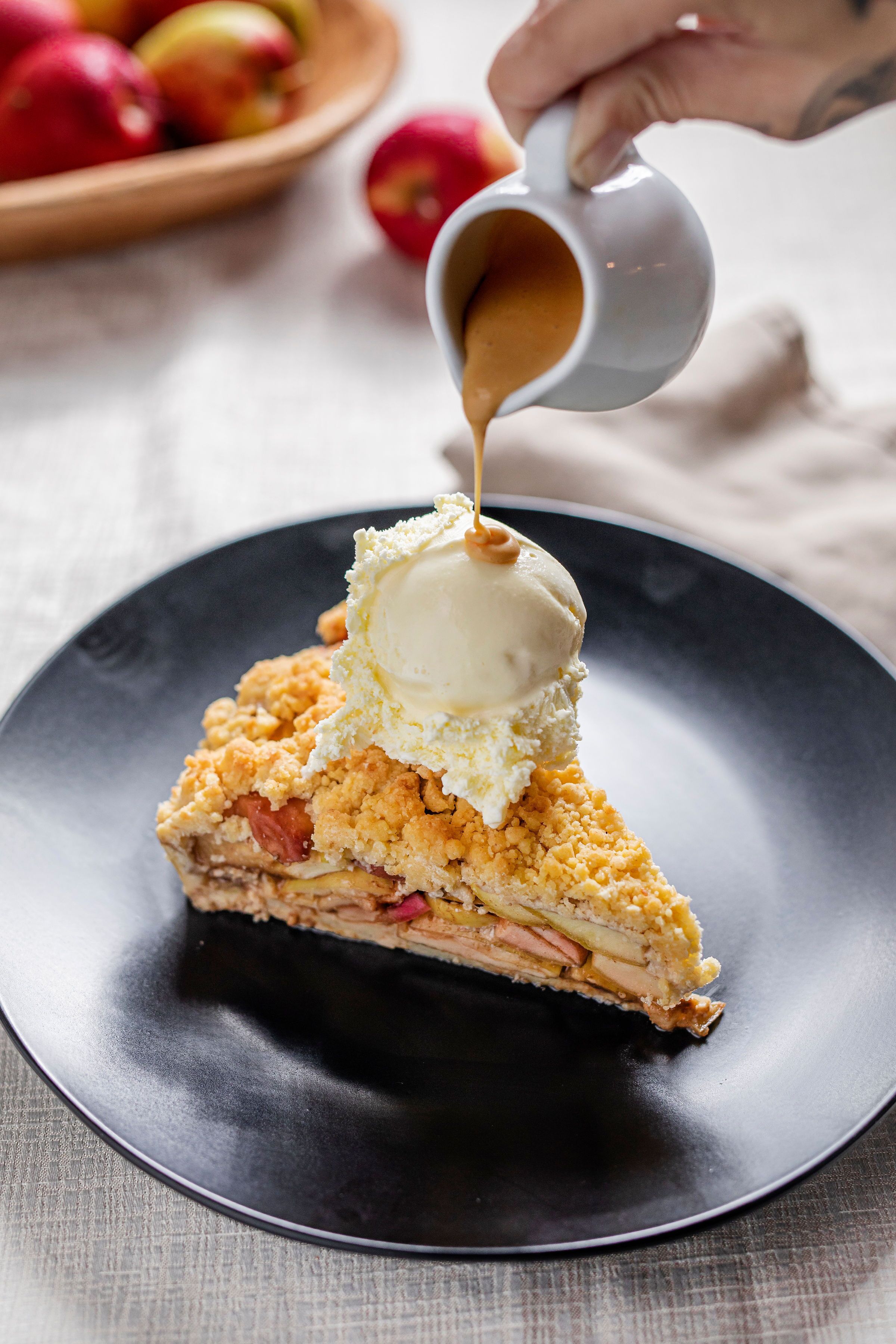 A slice of apple pie with ice cream on a black plate.