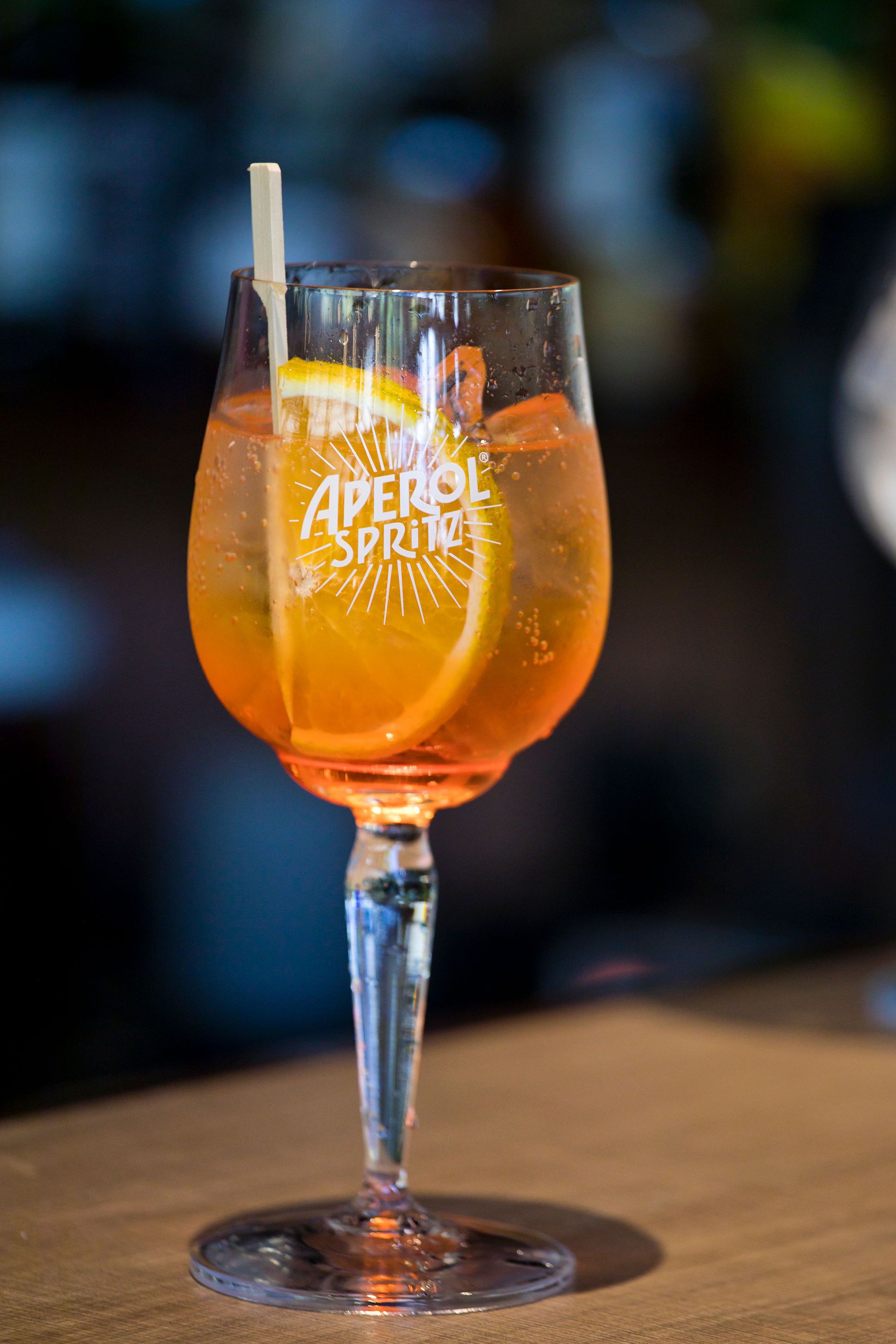 A glass with a straw and a slice of orange, labeled "Aperol Spritz."