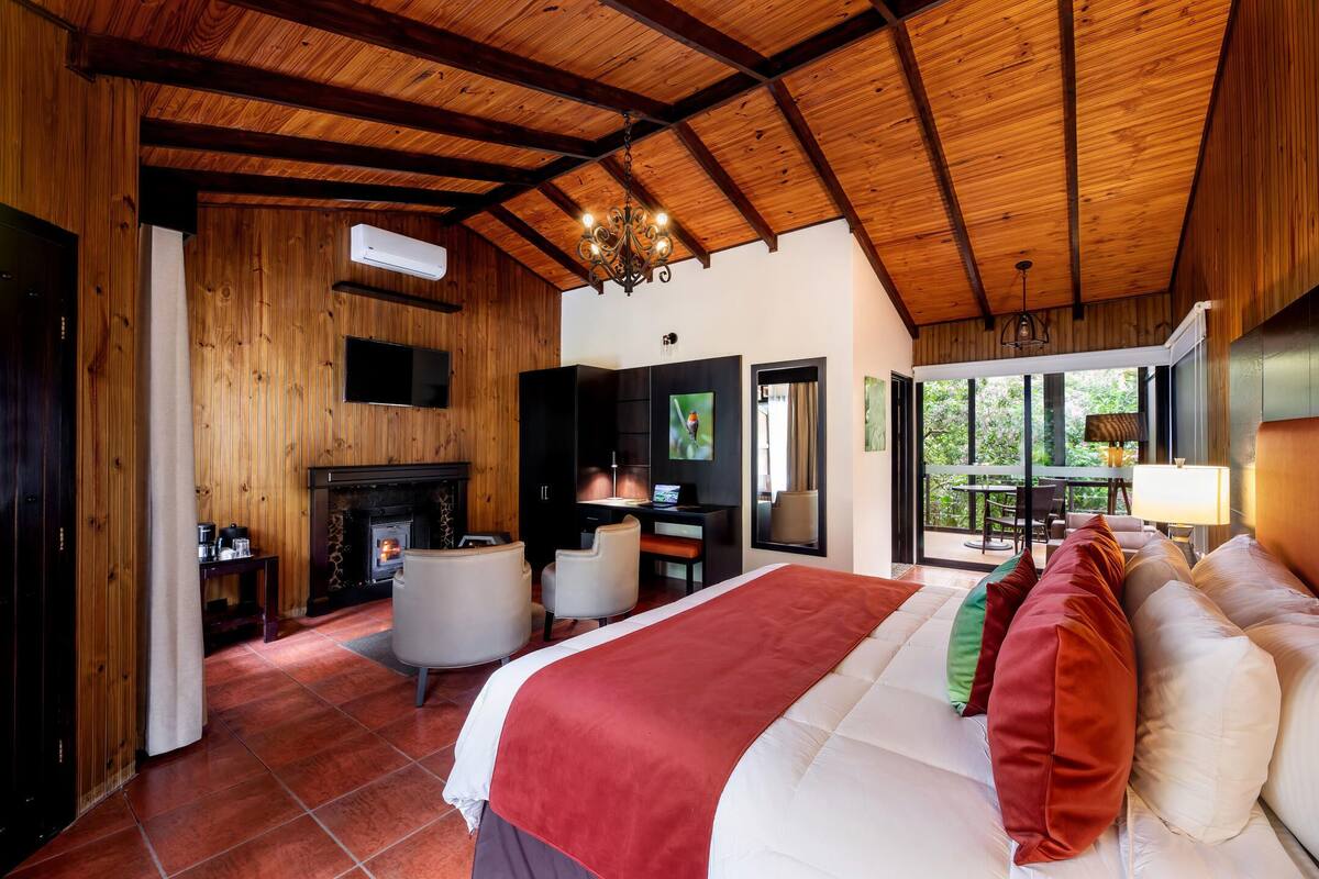 Quarto espaçoso com uma cama grande, lareira, escrivaninha e vista para o exterior.