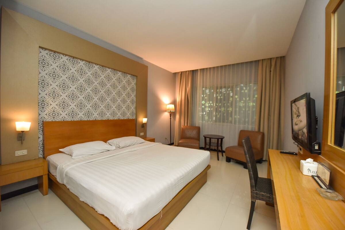 Ein Hotelzimmer mit einem großen Bett, einem Schreibtisch mit Stuhl, einem kleinen Tisch und einem Fernseher.