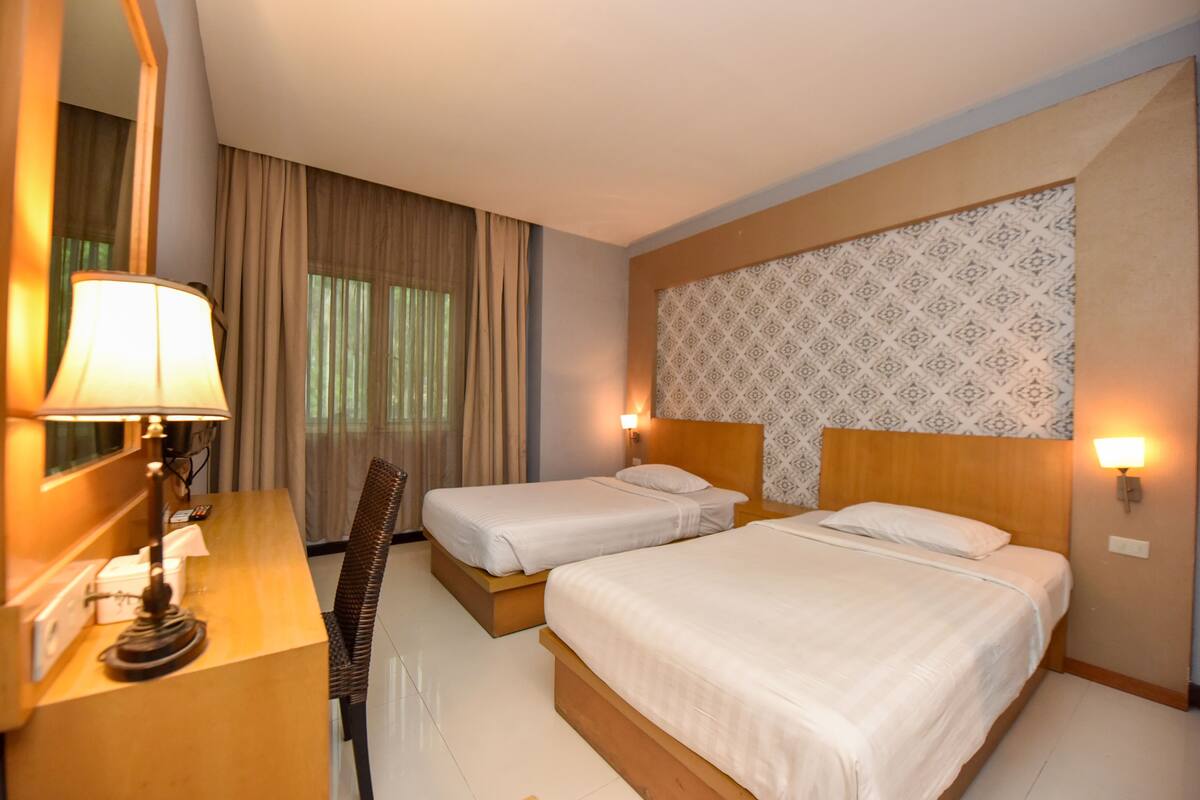 Ein Hotelzimmer mit zwei Betten, einem Schreibtisch mit Lampe, einem Stuhl und einem großen Spiegel.