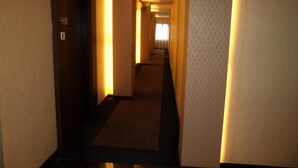 Un couloir d’hôtel avec des revêtements de sol et des murs recouverts de moquette, menant à une chambre dotée d’une fenêtre.