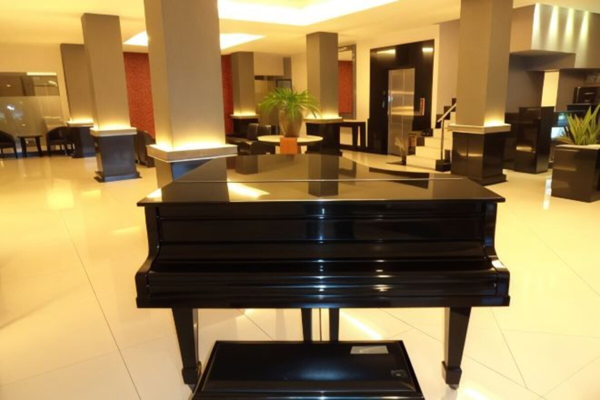 A grand piano in a well-lit lobby with modern decor, including large pillars and a potted plant.