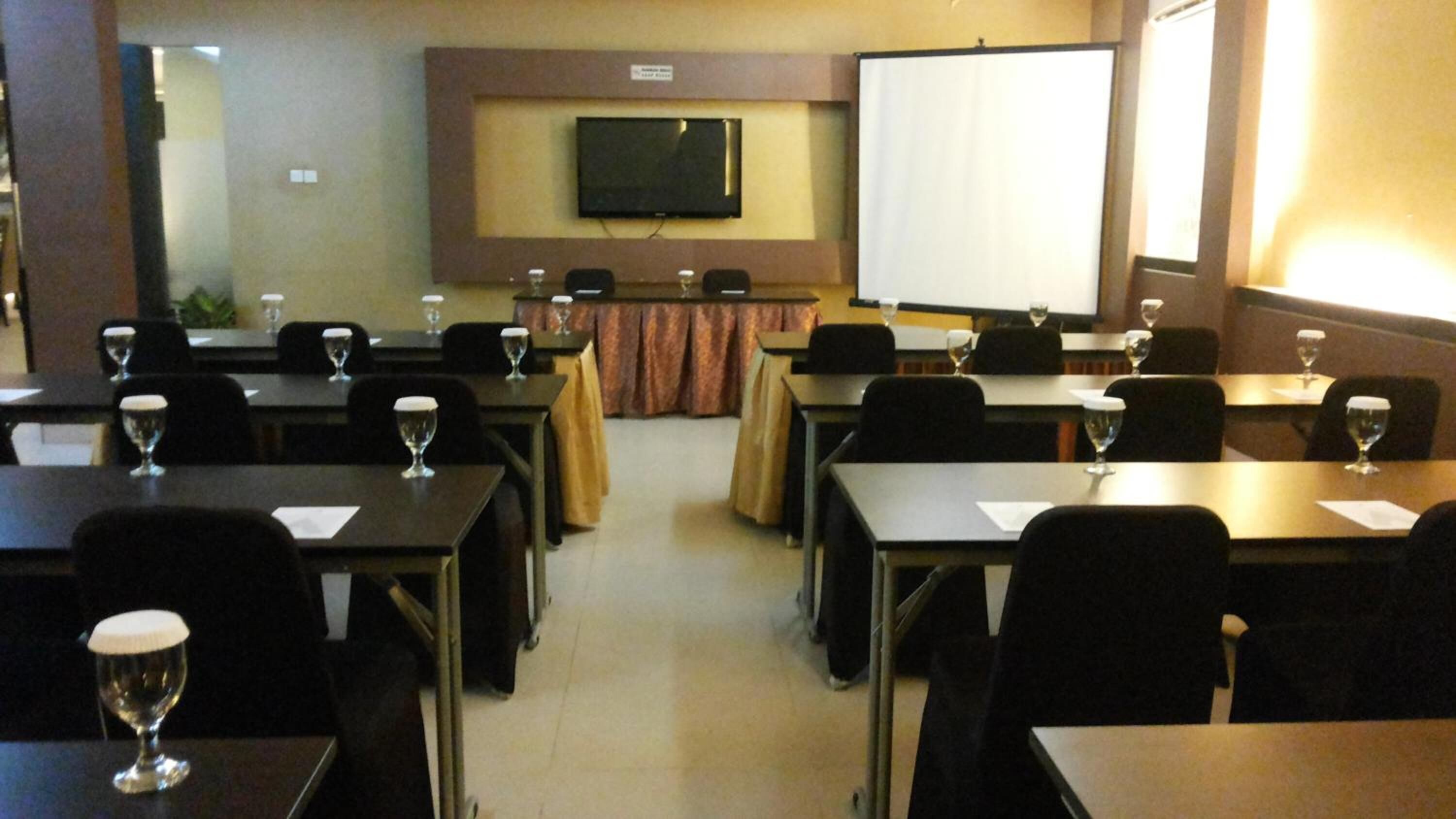 A conference room with tables, chairs, and a large screen.