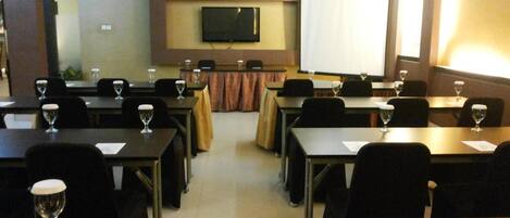 A conference room with tables, chairs, and a large screen.