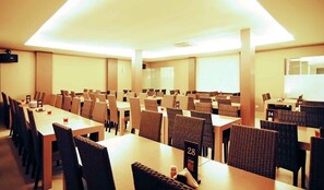 Une salle de conférence équipée de plusieurs tables et chaises, avec des places numérotées et un grand écran à l’avant.