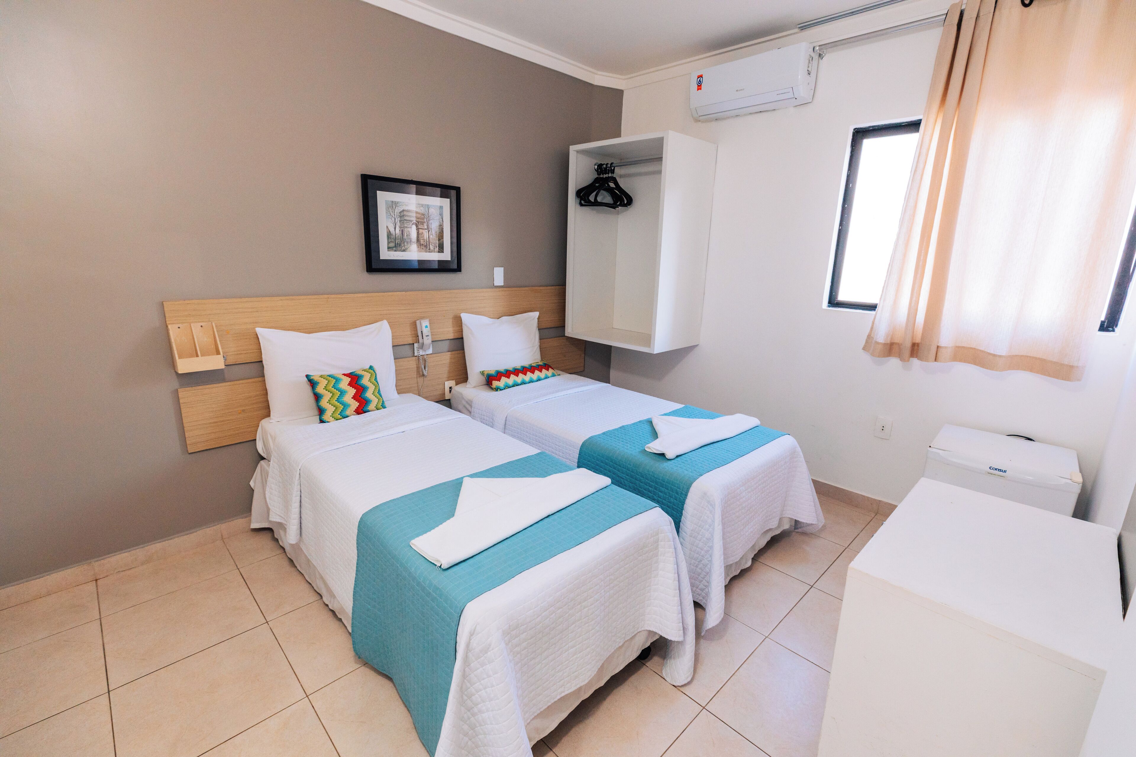 A hotel room with two beds, a wardrobe, a small desk, and a window with curtains.