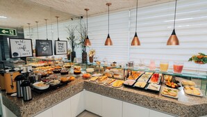 Un bufé con diversas opciones de comida y bebidas, una máquina de café y un cartel con un mensaje.
