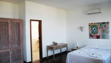 Una habitación de hotel con una cama, un armario de madera, una mesita con un jarrón, un cuadro en la pared y un equipo de aire acondicionado.