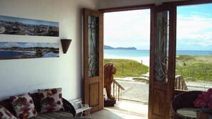 Une pièce avec vue sur la plage et l’océan, une porte en bois, un banc et un luminaire fixé au mur.