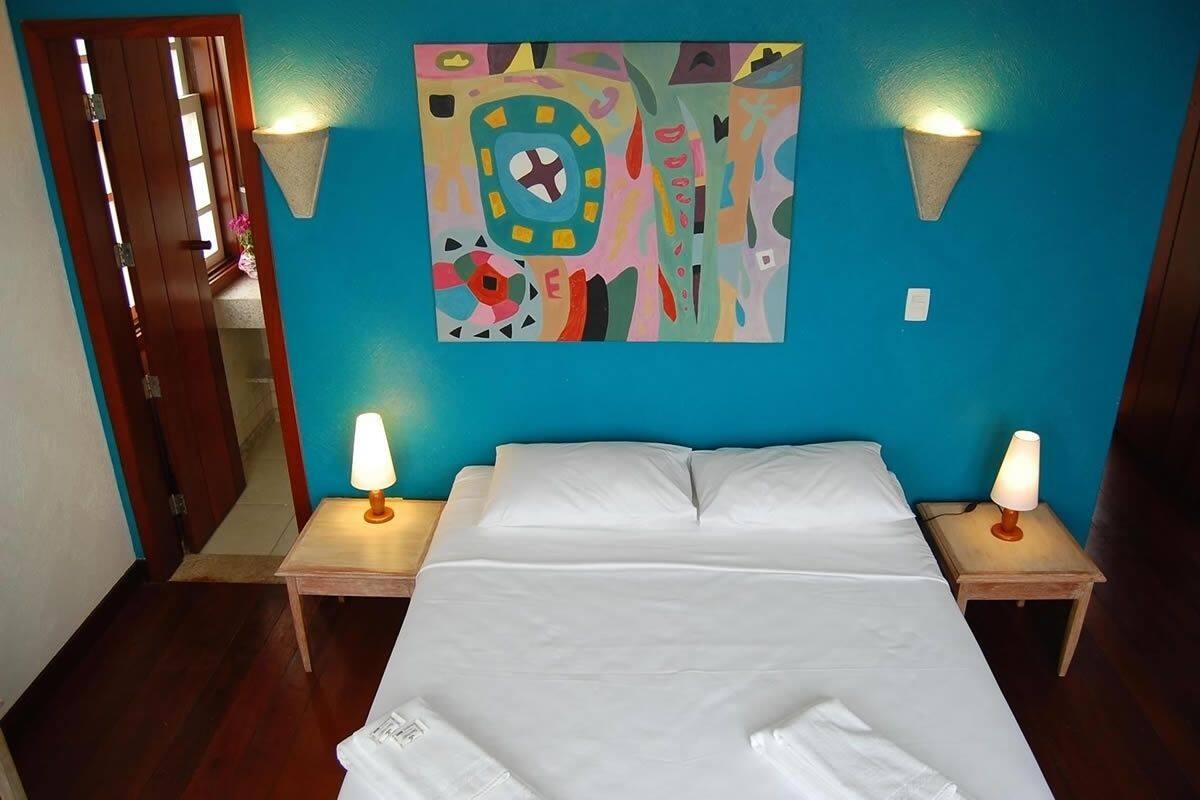 A bedroom with a bed, two bedside lamps, a colorful abstract painting on the wall, and a wooden door.
