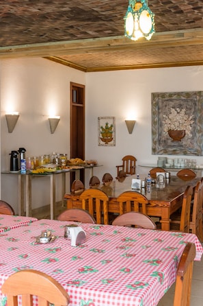 Un comedor con mantel a cuadros, sillas de madera, una mesa con cubierta de vidrio, luces fijadas a la pared y un cuadro.