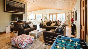 A cozy living room with leather sofas, a coffee table, and a foosball table. There is a painting on the wall and a TV on a stand. - Maria's Creekside B&B (Anchorage)