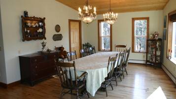 A dining room with a long table, wooden chairs, chandeliers, and a wooden cabinet with dishes.