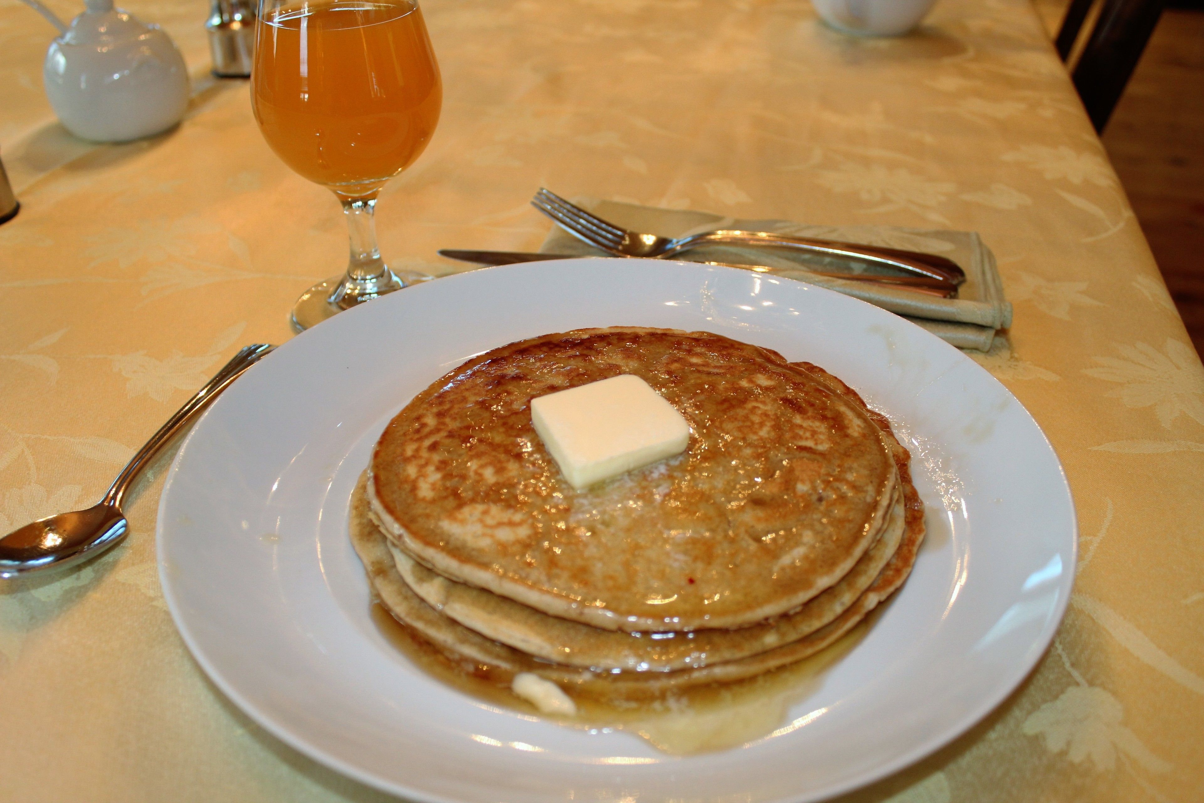 En tallrik med pannkakor och en klick smör, placerad på ett bord tillsammans med en tekanna och ett glas te.