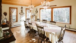A dining room with a wooden ceiling, large windows, and a chandelier. - Maria's Creekside B&B (Anchorage)