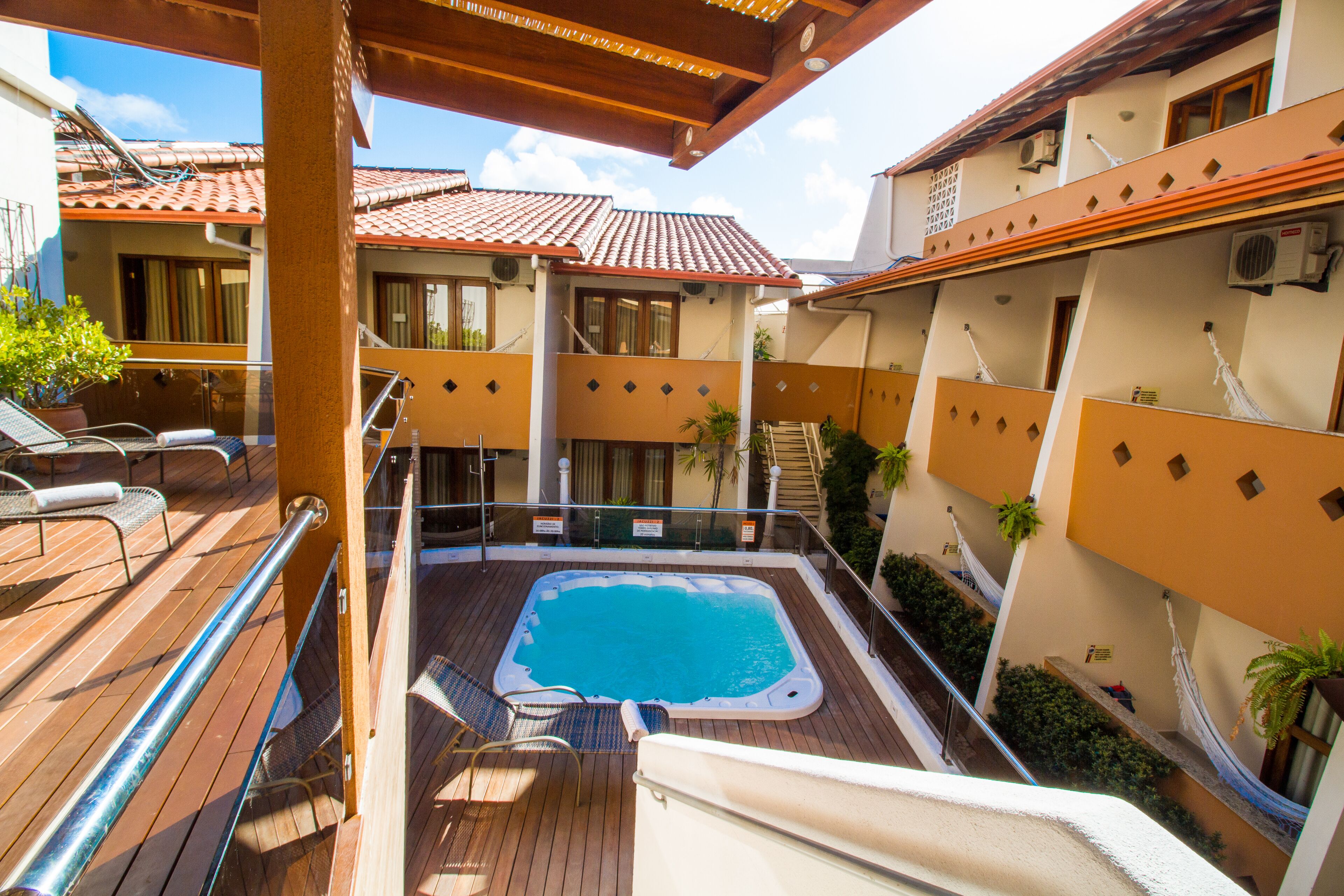 Una piscina en la azotea con un deck de madera, sillones de descanso y una zona cubierta con pérgola.