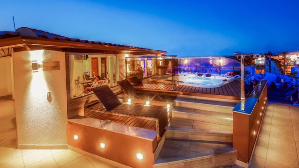 A well-lit outdoor area with a hot tub, wooden seating, and a pool. - Rede Andrade Terra Brasil (Porto Seguro)