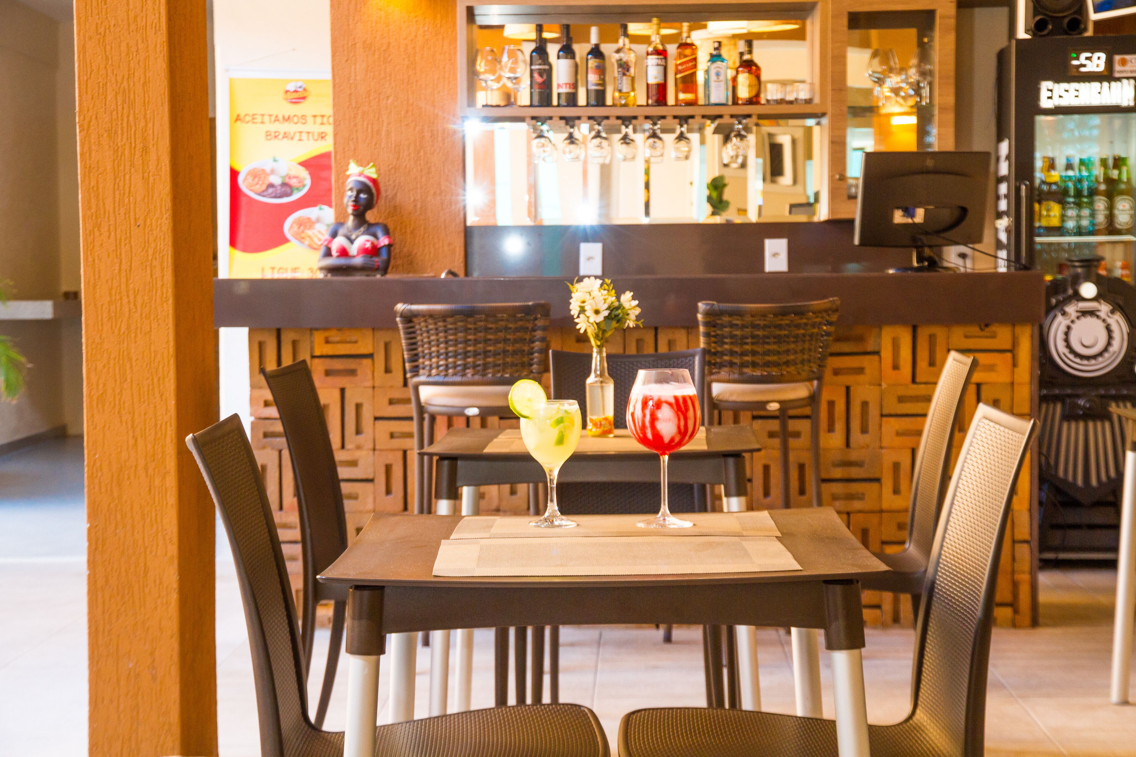 A restaurant with a bar area, wicker chairs, and a table with two drinks.
