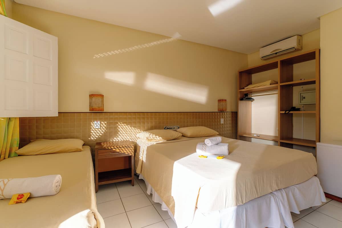 A hotel room with two beds, a wardrobe, a bedside table, and a built-in air conditioning unit.