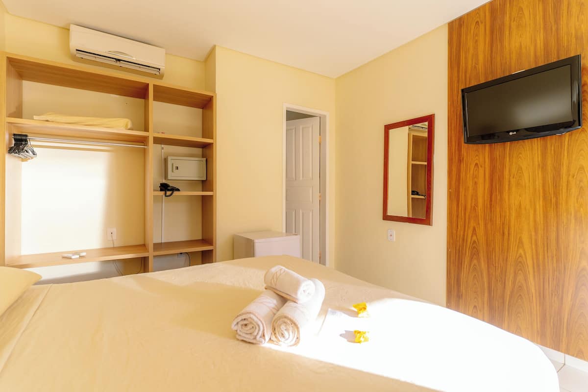 A hotel room with a bed, a TV mounted on the wall, a wardrobe, and a bathroom door.
