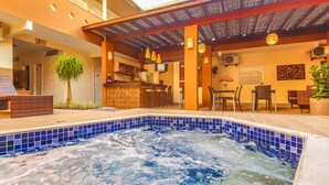 A hot tub area with a tiled pool, wooden seating, and a bar with a counter and chairs. - Rede Andrade Terra Brasil (Porto Seguro)