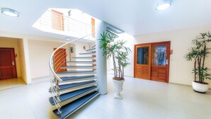 A modern interior with a spiral staircase, potted plants, and a wooden door. - Rede Andrade Terra Brasil (Porto Seguro)