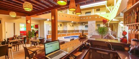 Un hall d’hôtel moderne doté d’un bar, d’un espace repas et offrant une vue sur la piscine.